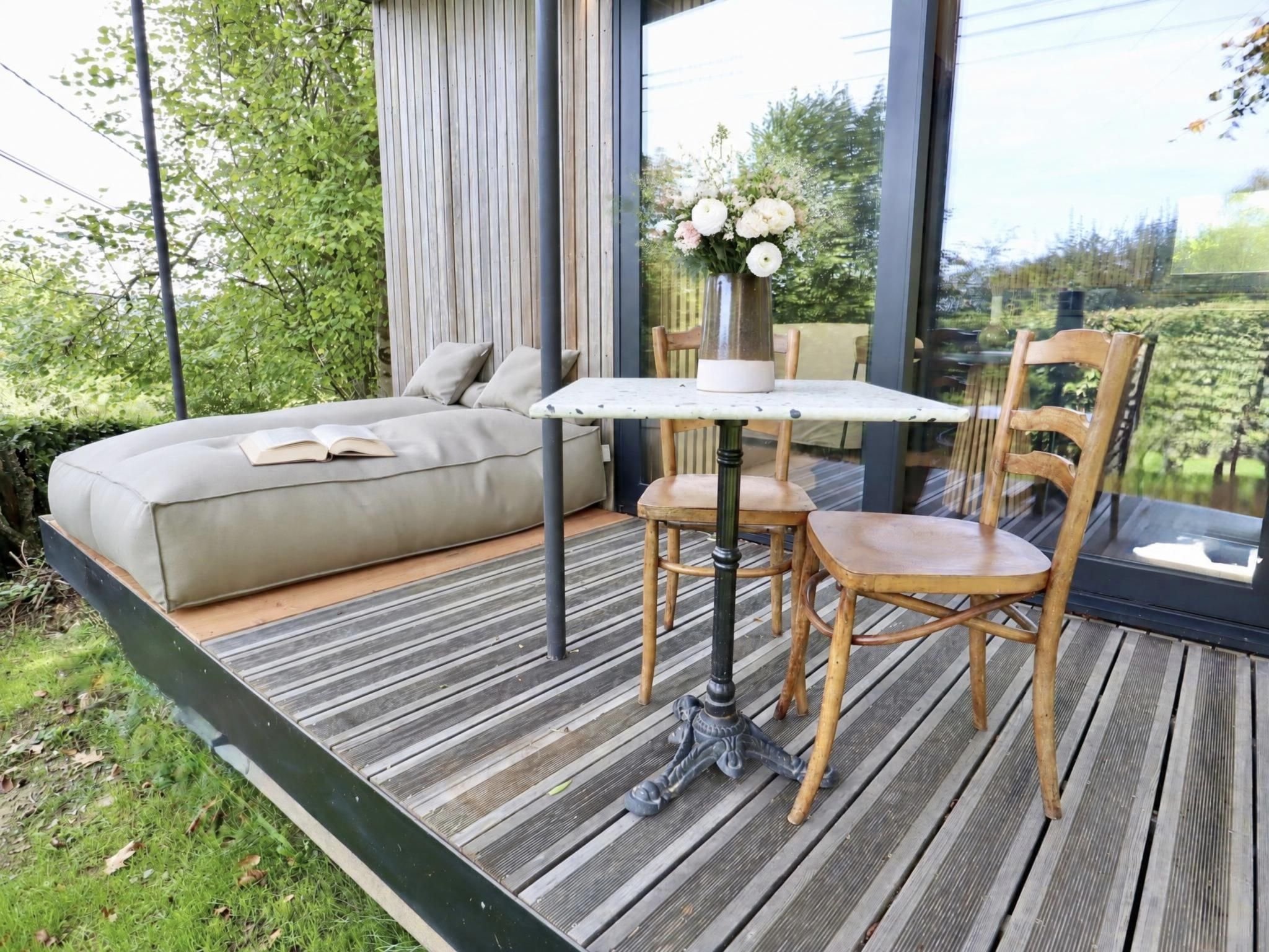 Een moderne zithoek buiten, met een bank, een tafel en stoelen, met uitzicht op een tuin.