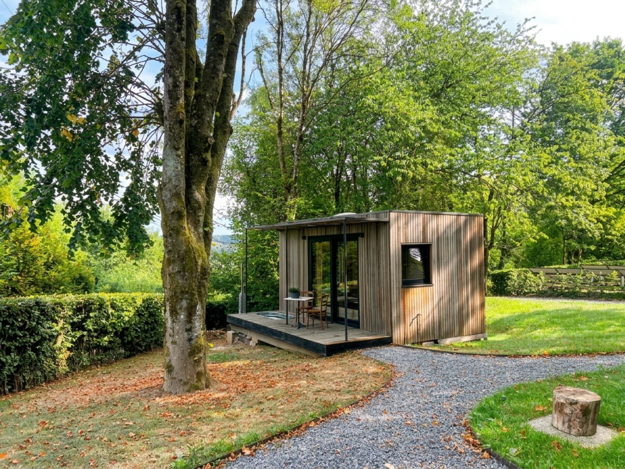 A modern wooden cabin with a glass door, a small deck, and a gravel path leading to it.