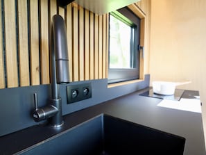 Een moderne keuken met een zwart aanrecht, een roestvrijstalen spoelbak en een raam met uitzicht op groen.