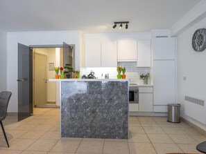 A modern kitchen with a marble island, white cabinets, and a small dining area. - Ground-floor apartment for 6 people (Middelkerke)