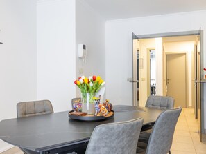 A modern dining area with a dark marble table, grey upholstered chairs, and a vase of tulips. - Ground-floor apartment for 6 people (Middelkerke)