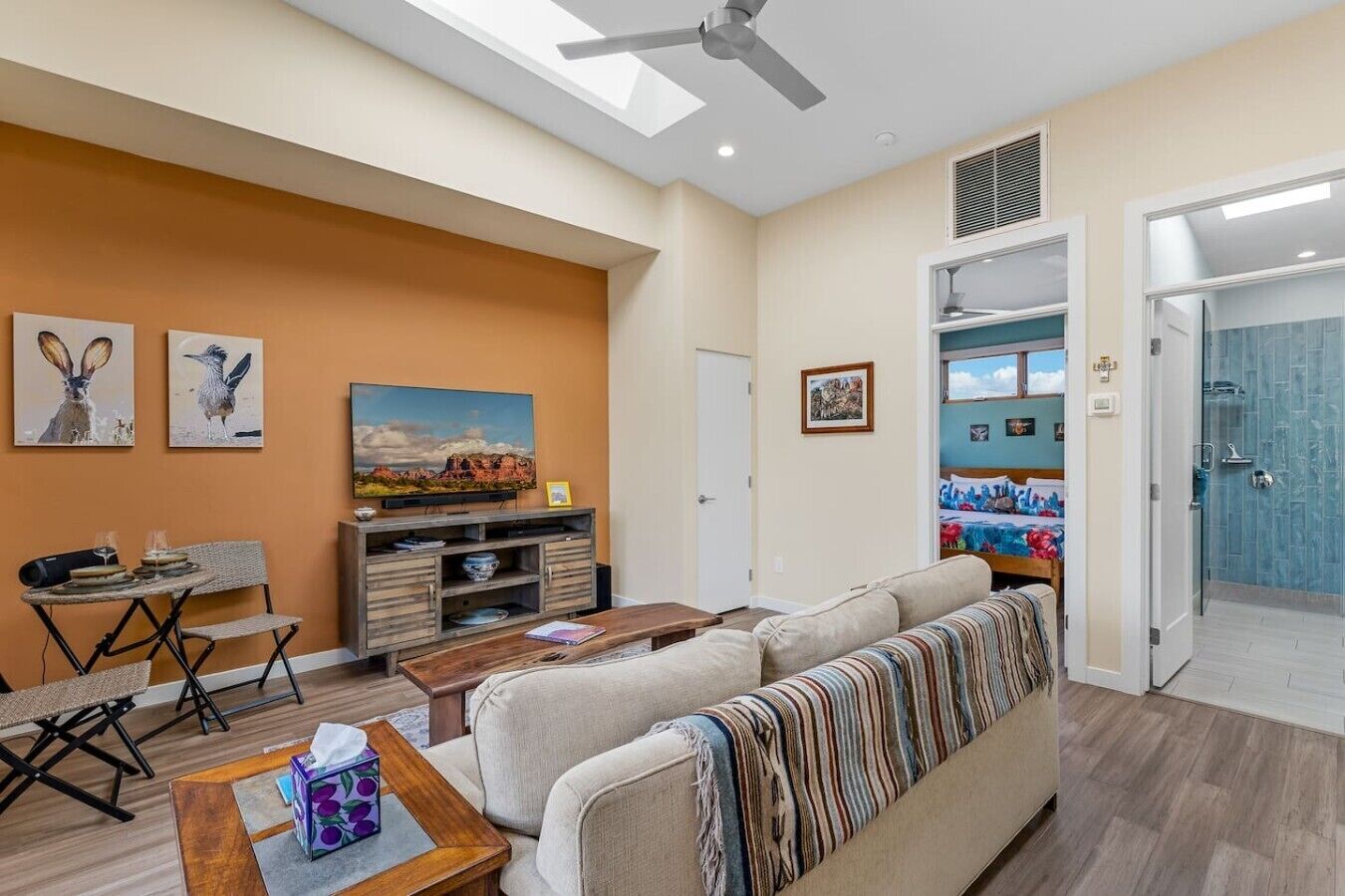 A living room with a sofa, coffee table, and entertainment unit. There is a door leading to a bathroom with a shower.