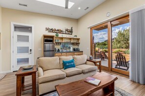 A living room with a sofa, coffee table, and a view of the outdoors through a sliding glass door. - Rancho Rojo Casita - Kitchenette, Laundry, Views (Sedona)
