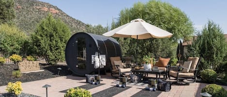 Un patio al aire libre con un barril, asientos y una sombrilla grande.