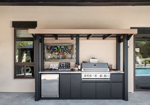 An outdoor kitchen with a gas stove, a sink, and a window with a floral painting. - Desert Bloom - Heated Pool & Spa, Sauna, Gym, Game Room (Sedona)