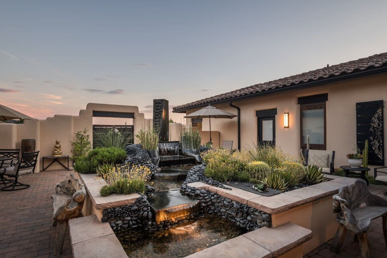 Un patio con fuente de agua, mobiliario exterior y un edificio con techo de tejas.
