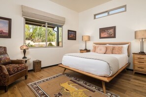 A bedroom with a bed, a chair, a nightstand, a lamp, a window, and a rug. - Desert Bloom - Heated Pool & Spa, Sauna, Gym, Game Room (Sedona)