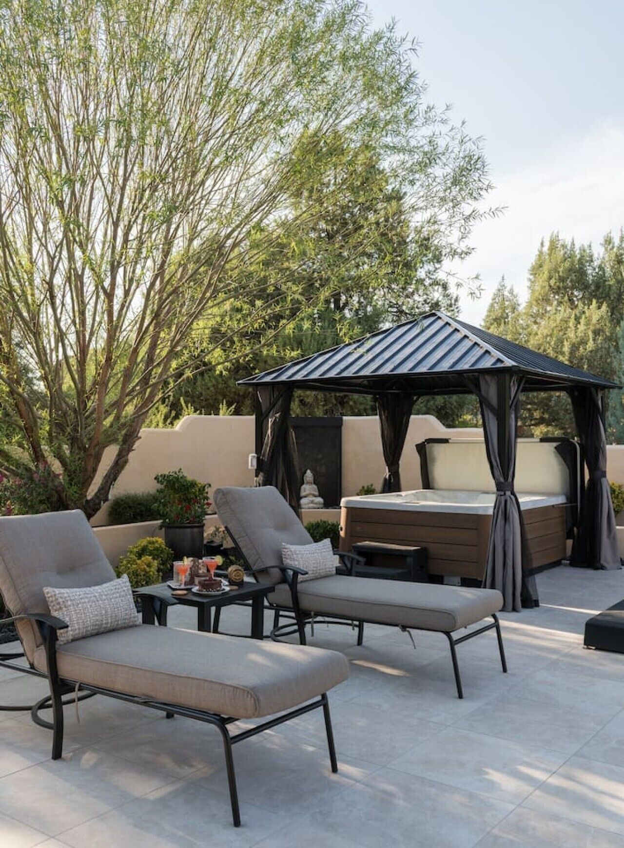Een terras met twee loungestoelen, een tafeltje met drankjes en een hottub onder een pergola.