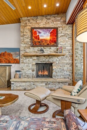 A stone fireplace with a television above it, a sofa, and a rug. - Rojo Retreat - Main 2BR Unit, Hot Tub, Patio (Sedona)