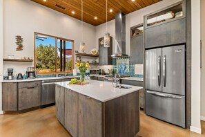 A modern kitchen with a central island, stainless steel appliances, and a view of the outdoors. - Rojo Retreat - Main 2BR Unit, Hot Tub, Patio (Sedona)