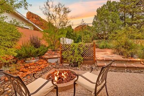 Eine Außenpatio-Terrasse mit Feuerstelle, zwei Stühlen, einem Holzzaun und verschiedenen Pflanzen.