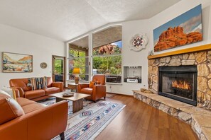 Ein Wohnzimmer mit Ledersofas, einem Kamin aus Stein und einem großen Fenster mit Blick auf Grünflächen.