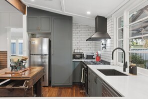 A modern kitchen with grey cabinets, a stainless steel refrigerator, a gas stove, and a black range hood. - Kalamunda Cottage (Kalamunda)