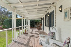 A covered porch with a wooden deck, white railings, and a table with chairs. - Kalamunda Cottage (Kalamunda)