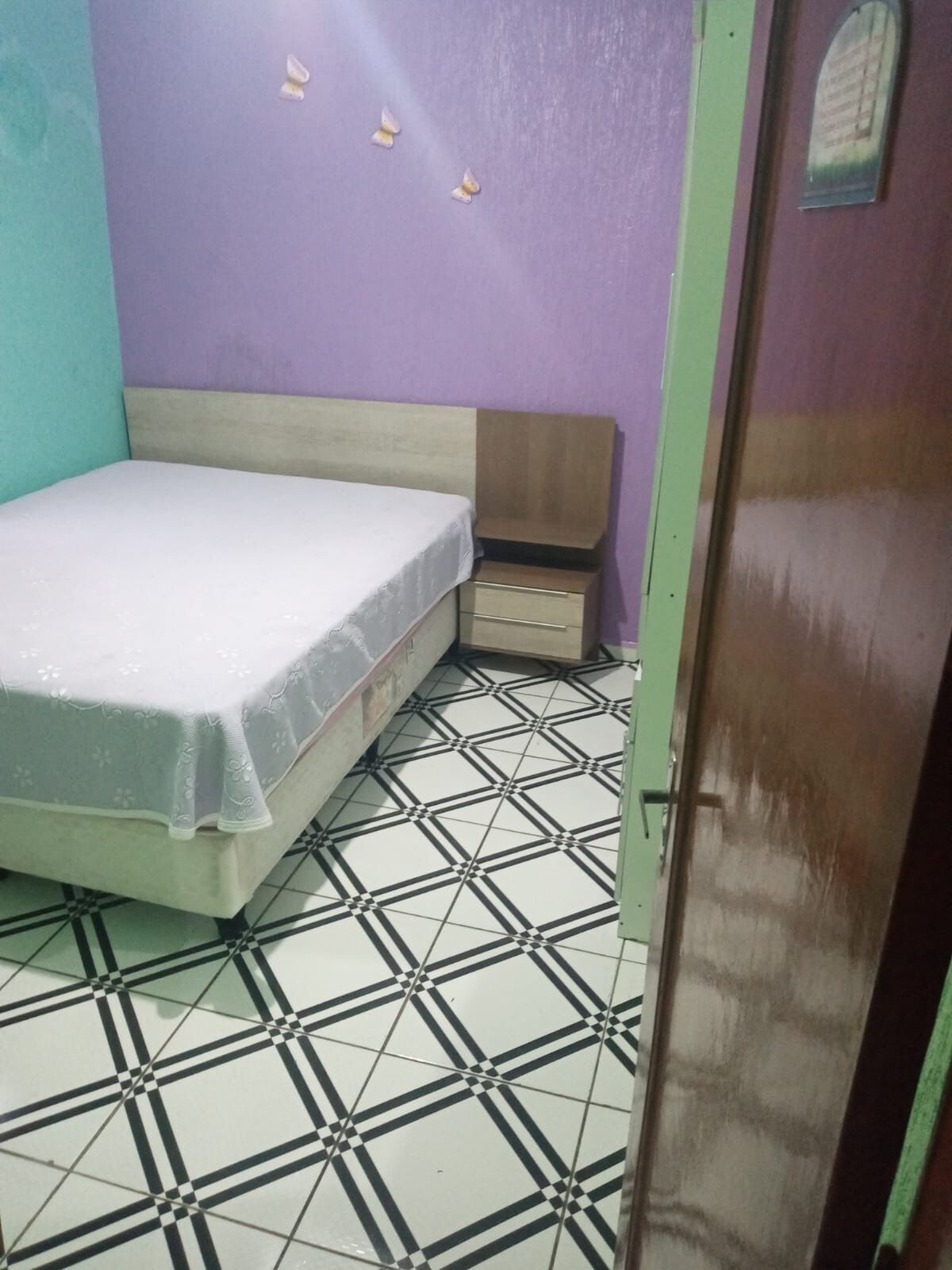 Una habitación con una cama, una mesita de noche pequeña y un aplique de pared.