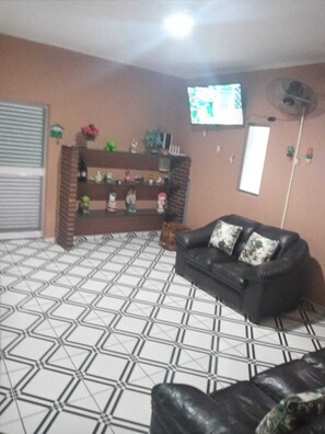 A living room with a black leather sofa, a patterned floor, a TV mounted on the wall, and a brick fireplace. - House with pool facing the sea in Itanhaém (Itanhaém)