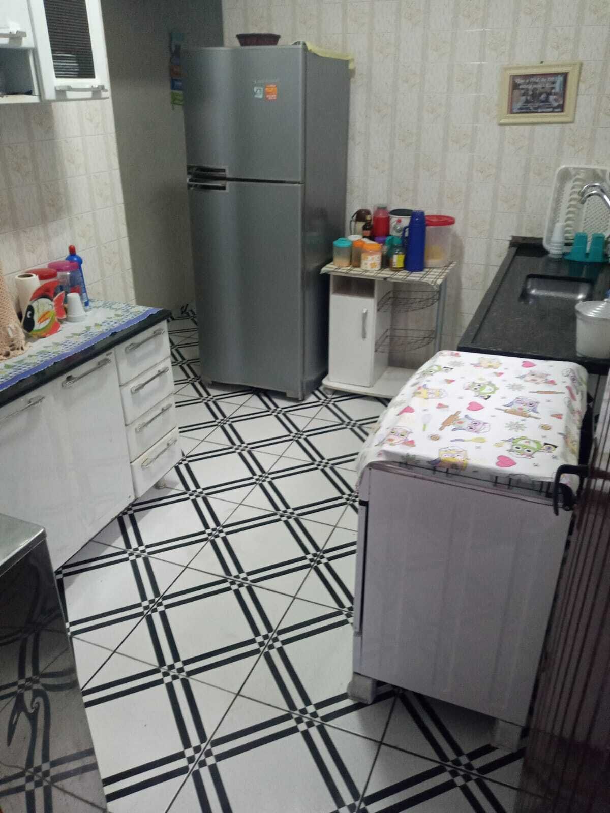 Cocina compacta con refrigerador, pileta y microondas. El piso presenta un diseño particular y un mueble pequeño con diversos objetos encima.
