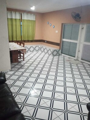 A room with a tiled floor, a dining table with chairs, a window with curtains, and a wall-mounted fan. - House with pool facing the sea in Itanhaém (Itanhaém)