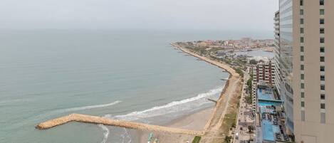 Eine Küstenstadt mit Strand, einer Promenade gesäumt von Sonnenschirmen und hohen Wolkenkratzern.