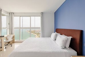 Ein Hotelzimmer mit einem großen Bett, einem Schreibtisch und Meerblick.