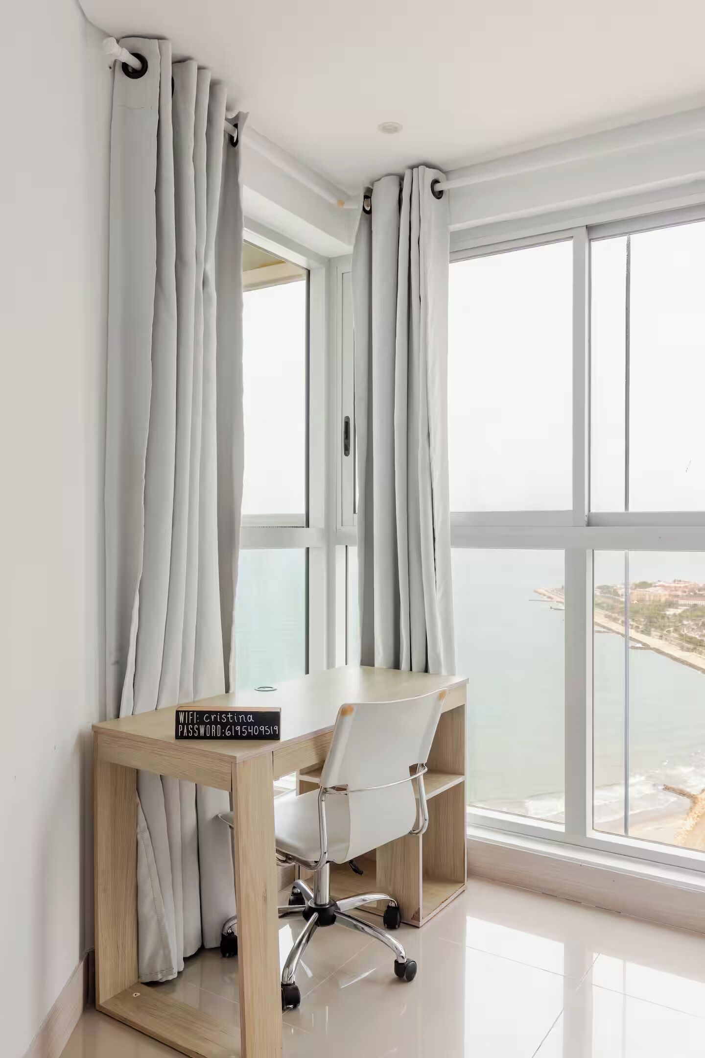 A modern office space with a desk, chair, and a view of the sea through large windows.