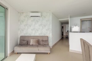Ein modernes Wohnzimmer mit einem grauen Sofa, einer weißen Klimaanlage und einem Küchenbereich im Hintergrund.