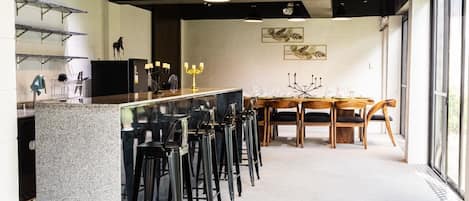 A modern bar area with a granite countertop, black bar stools, and pendant lighting.