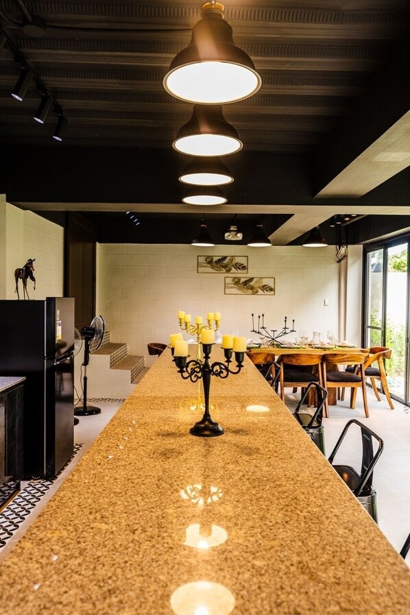 Cocina moderna con una barra alargada, iluminación colgante y comedor con mesa preparada para cuatro.
