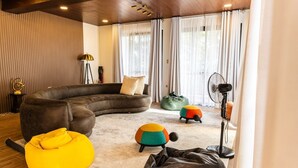 Ein modernes Wohnzimmer mit einem gebogenen Ecksofa, einem gelben Sitzsack und farbenfrohen Hocker.