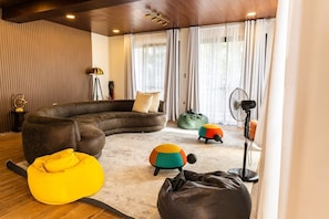 Een moderne woonkamer met een gebogen modulaire bank, een gele relaxstoel en kleurrijke poefs.