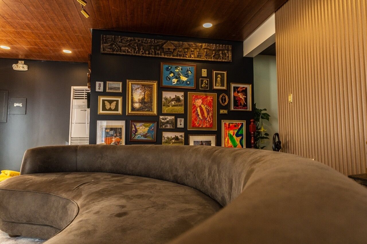 A room with a curved sofa, a wall adorned with various framed artworks, and a wooden ceiling.