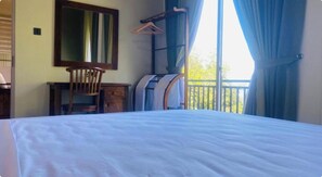 Habitación de hotel con cama, una silla, escritorio, espejo y balcón con cortinas.