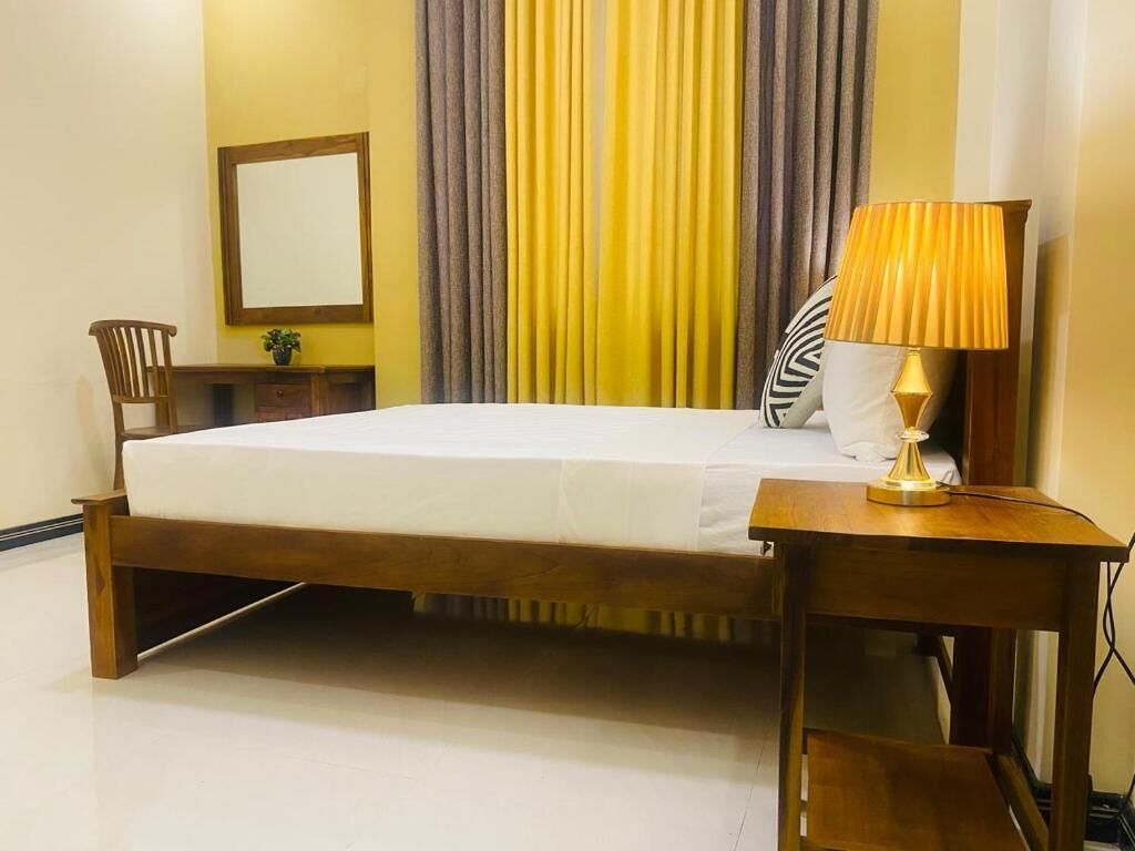 Une chambre d’hôtel avec un lit, une table de chevet, une lampe, une chaise, un miroir et des rideaux.