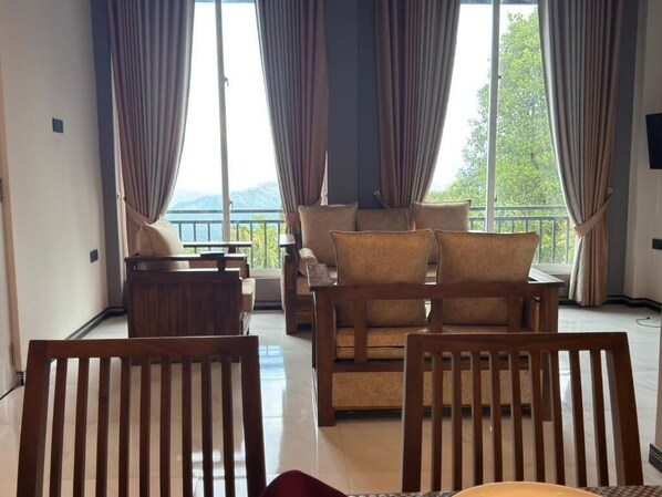A room with a sofa set, wooden chairs, and a view of a balcony with curtains.