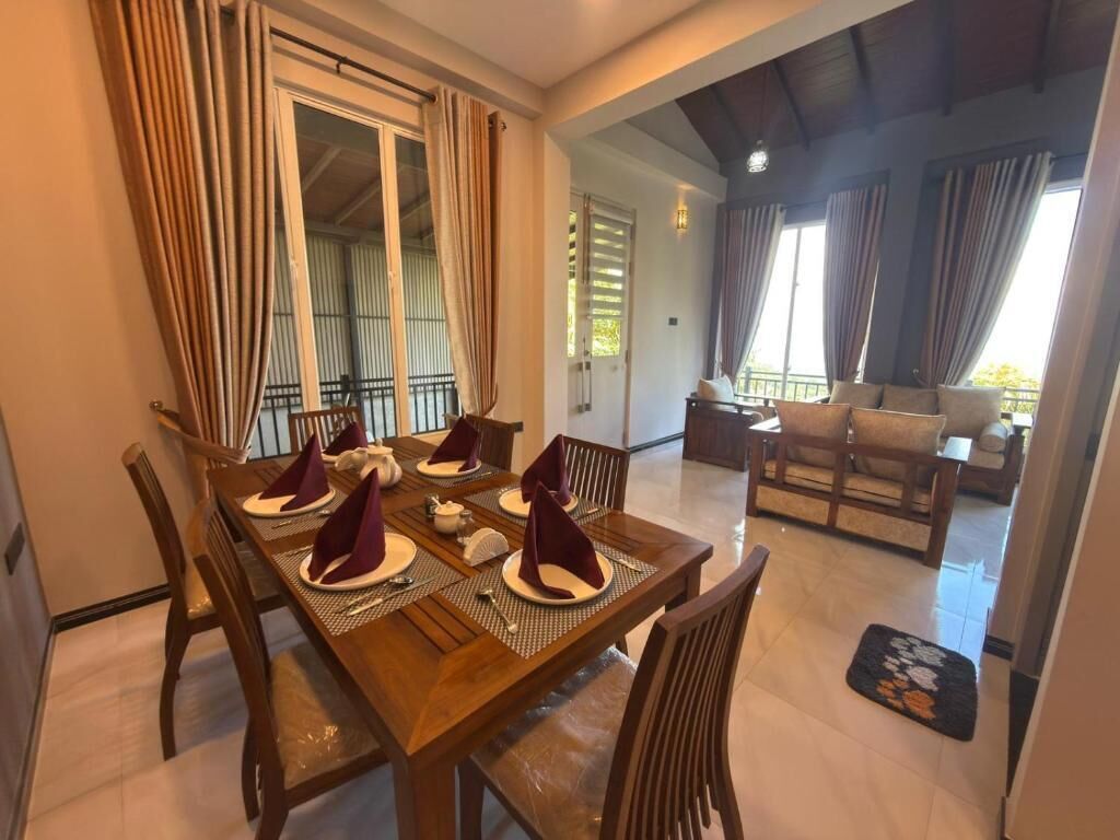 A dining area with a wooden table set for four, chairs, and a sofa in the background.