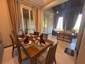 A dining area with a wooden table set for four, chairs, and a sofa in the background. - Sunrise Villa (Nugaliyadda)