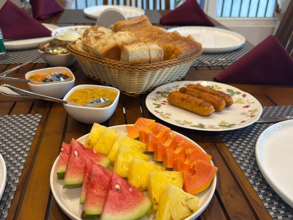 Une table à manger avec une assiette de fruits coupés, un panier de pain et une assiette de viennoiseries.