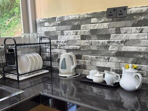 A kitchen with a black countertop, a stone backsplash, and a dish rack with plates and cups.