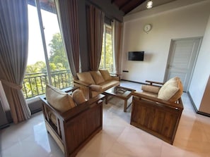 A spacious living area with a sofa set, a coffee table, and a TV mounted on the wall. - Sunrise Villa (Nugaliyadda)