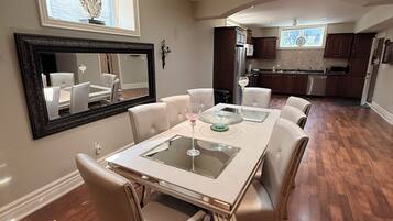 A dining area with a table and chairs, a kitchen in the background, and a ceiling with recessed lighting.