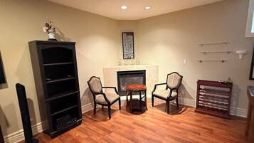 A room with a fireplace, two chairs, a bookshelf, and a small table.