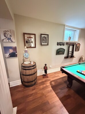 Una habitación con mesa de billar, suelo de madera y varias fotografías enmarcadas en las paredes.
