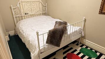 A single white metal bed in a room with a black and white striped carpet.