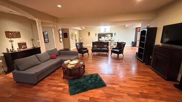A spacious living room with a grey sectional sofa, two black armchairs, a coffee table, and a television on a wooden cabinet.