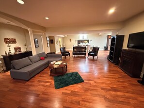 Un salón espacioso con un sofá seccional gris, dos sillones negros, una mesa de centro y un televisor sobre un mueble de madera.