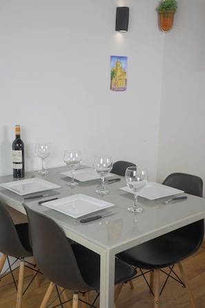 Una mesa de comedor con cuatro sillas, una botella de vino y cuatro copas preparadas para una comida.