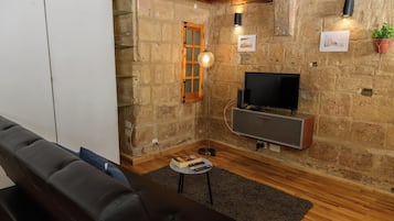 Una sala de estar acogedora con pared de piedra, techo de madera, sofá de cuero negro, televisor y una mesita con un libro y controles remotos.