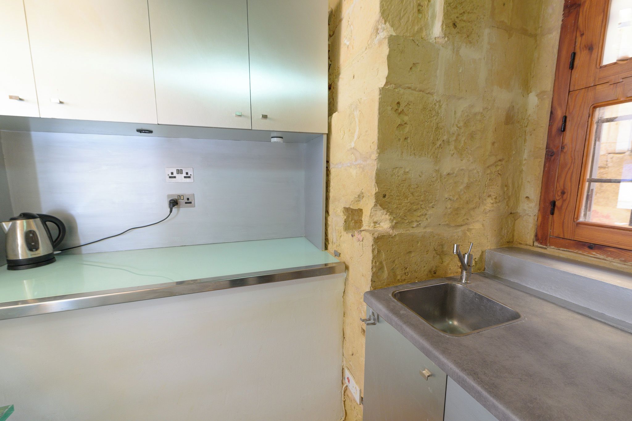 A small kitchenette with a sink, a kettle, and a countertop.
