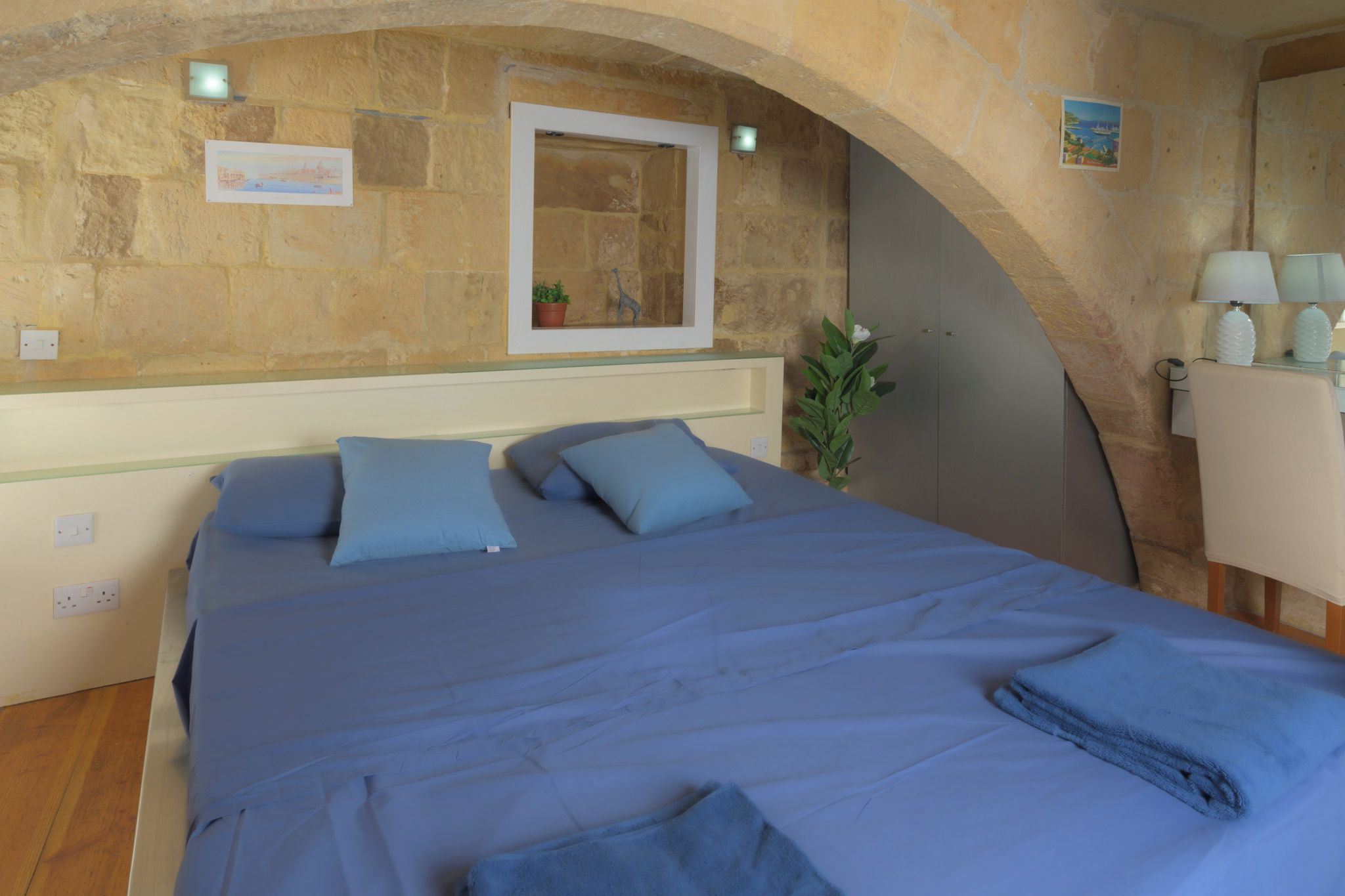 A bedroom with a large bed, a mirror, a potted plant, and a lamp.