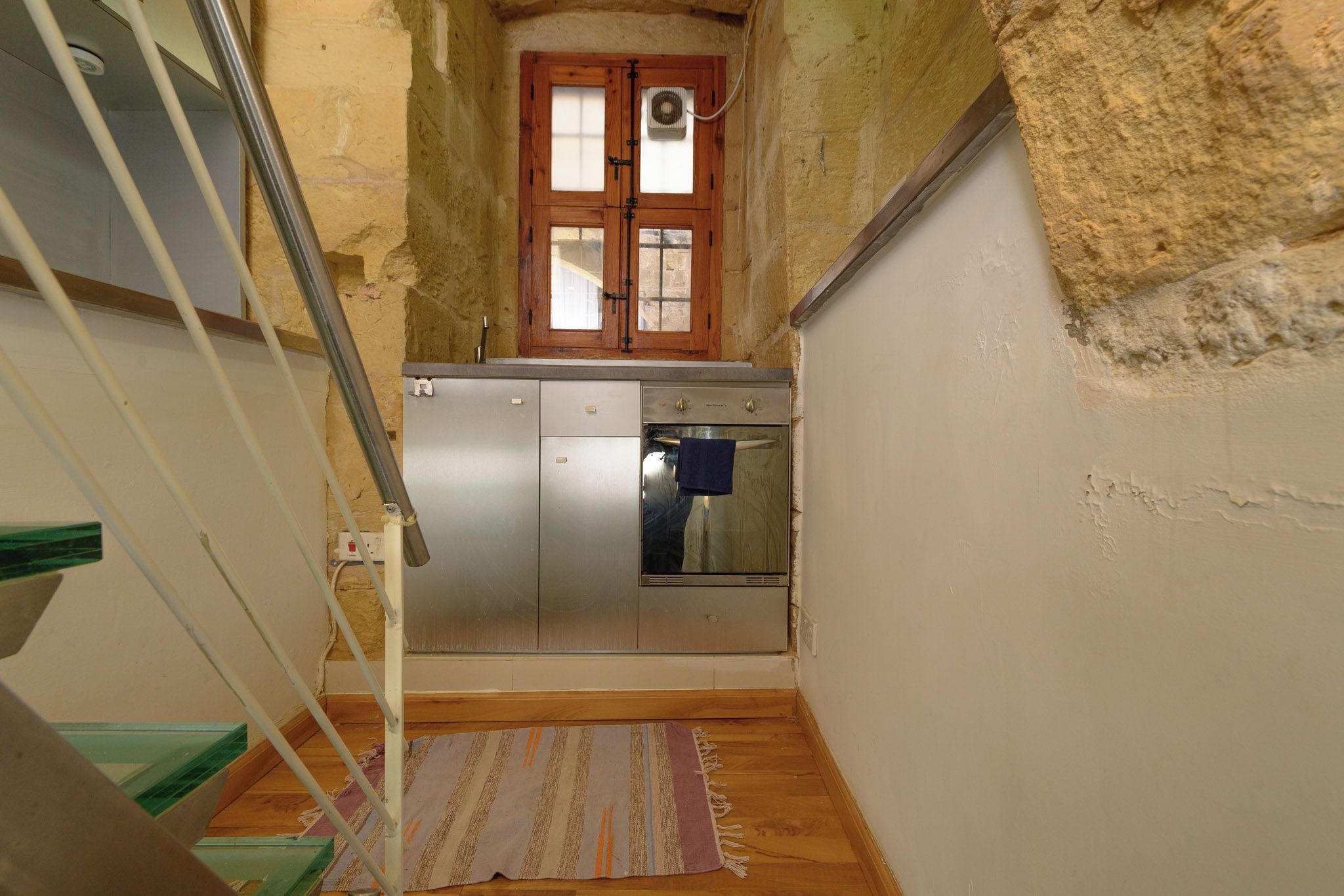 Eine schmale Treppe führt zu einer Küche mit einer Holztür und einem kleinen Fenster.